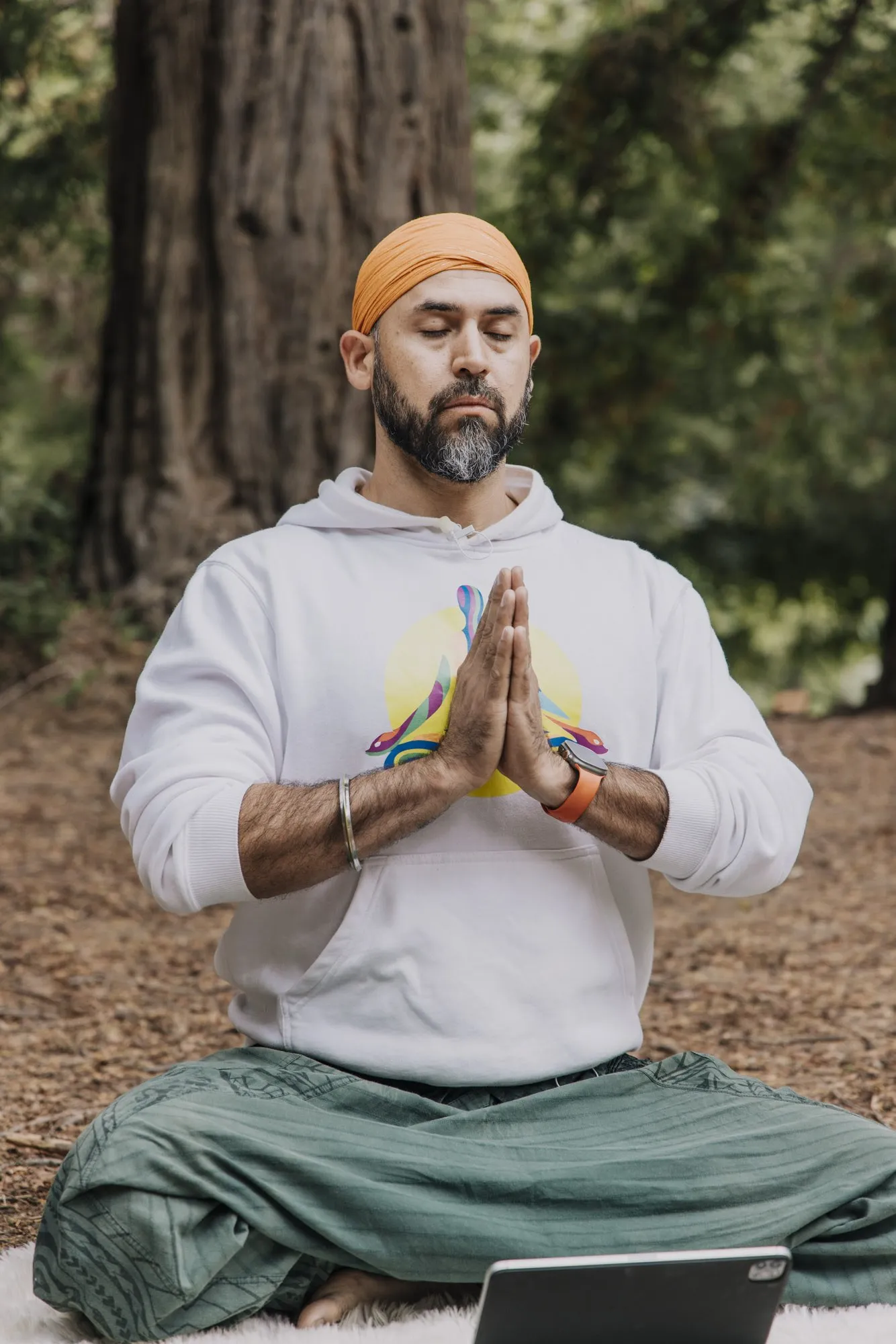 Italo meditando sentado en flor de loto en un bosque de secuoyas, con las manos juntas frente al pecho.