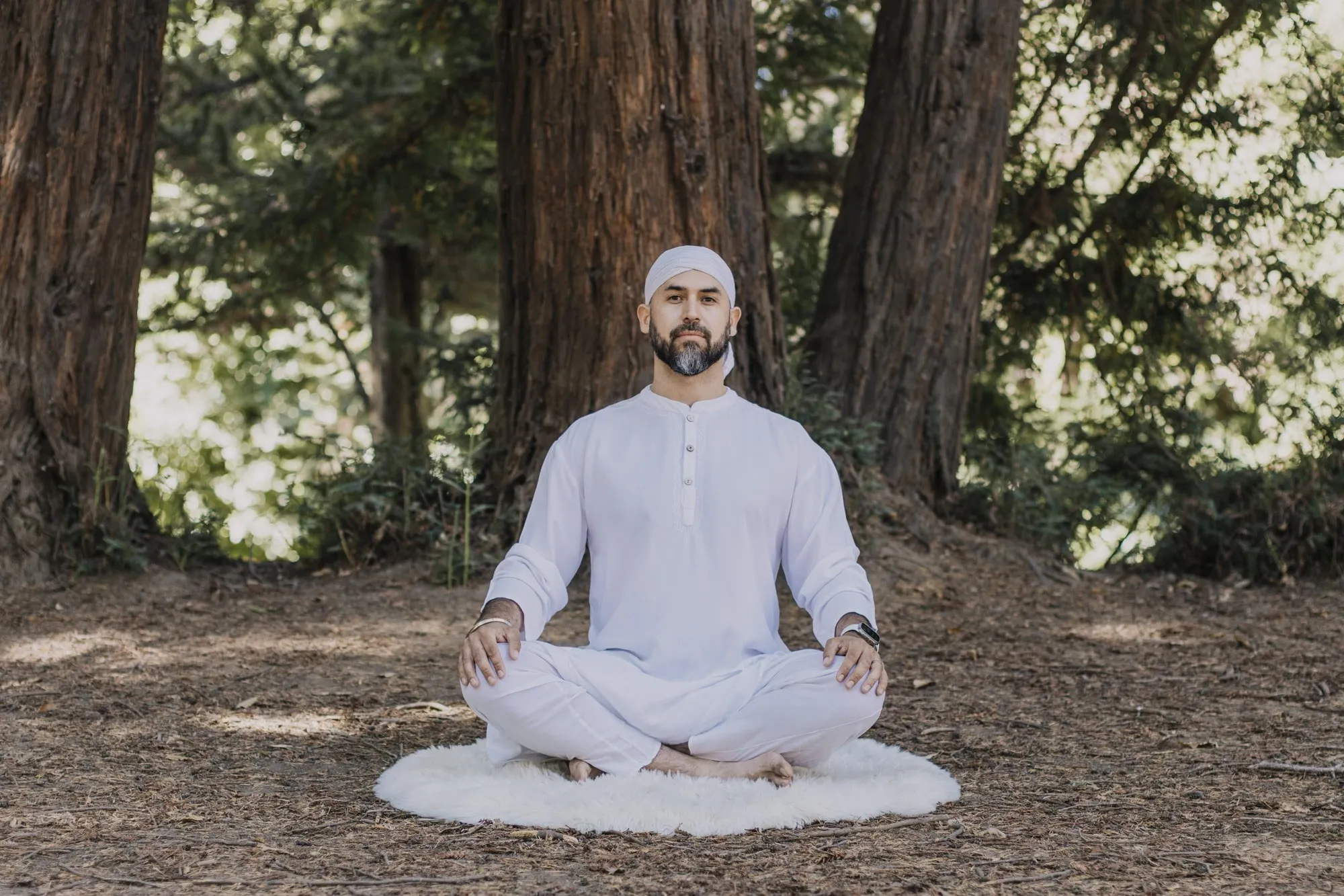 Plano abierto de Italo meditando sobre una manta blanca entre secuoyas.